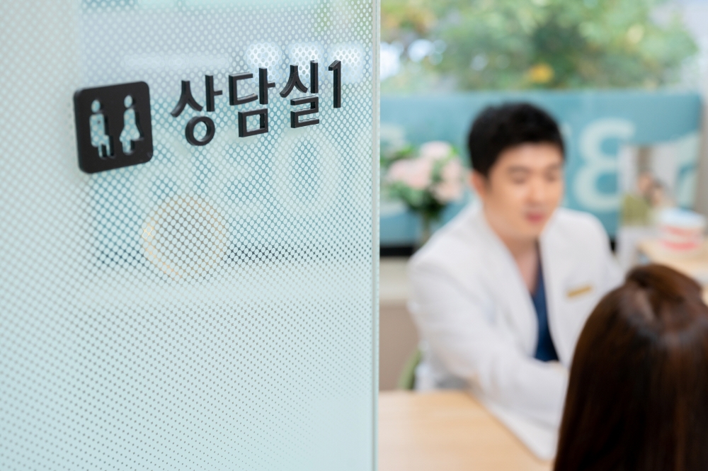 상담실1 안내 표지가 새겨진 반투명 유리 칸막이 너머로 의료진과 환자가 마주 앉아 있는 모습